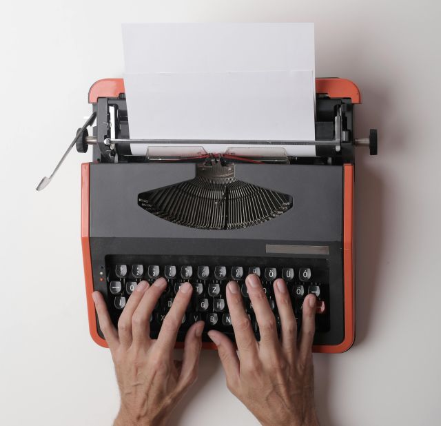 From above crop person using vintage black and red typewriter with white blank sheet of paper against white background